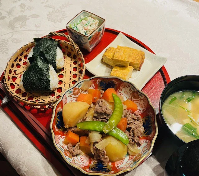 Basic Course: nikujaga, onigiri, dashimaki tamago, shiraae and miso soup on a red lacquer tray